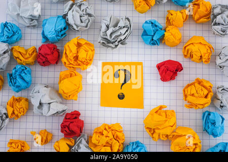 Colorful crumpled paper balls around yellow paper note with question mark. Close up. Stock Photo