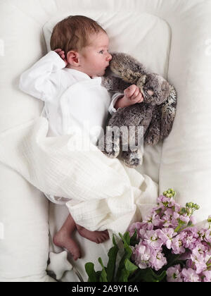 Newborn Baby Boy lying on bed and Sleeping with Teddy Bear. Baby needs his sleep. Flower decoration of kids bed Stock Photo