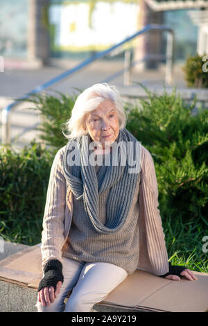 Poor aged woman sitting outside on her own Stock Photo
