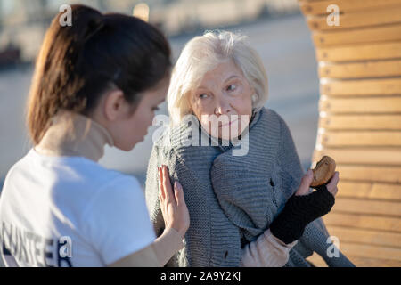 Dark-haired kind volunteer supporting aged homeless woman Stock Photo