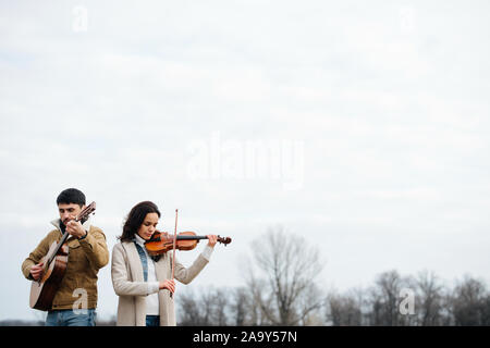 Two warmly dressed musicians playing in countryside at autumn over bright sky Stock Photo