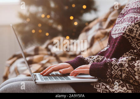 Woman in warm sweater using laptop over Christmas decorating room Stock Photo