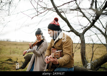 Two musicians sitting on a branch, playing music in a autumn countryside Stock Photo