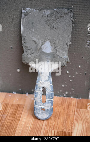 On the linoleum is a spatula leaning against the wall. Paint spatula in cement against the wall. Repair work for home insulation. Stock Photo