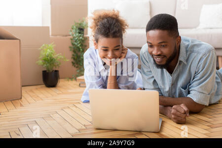 Black Spouses Using Laptop Lying On Floor Indoor Stock Photo