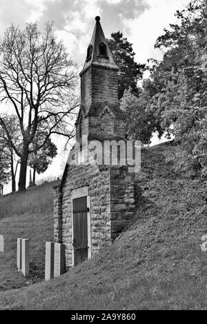 Very old mausoleum built into the side of a hill with steeple, tombstones, and wrought iron fence Stock Photo