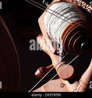 double drive flyer and bobbin with light grey yarn in a sunny spot with a dark room behind. Stock Photo