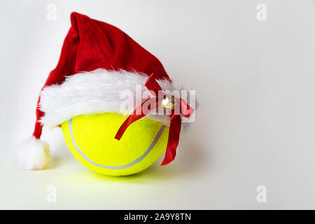 Christmas and New Year concept with Santa hat on tennis ball on gray background. Winter sport healthy layout. Holiday conception. Place for your text. Stock Photo