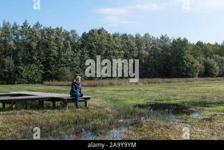 mature woman is resting in nature on a wooden platform in the Veluwe nature reserve in the Netherlands Stock Photo