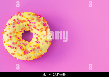 Icing donut on a pink background with text space. Flat lay, purple mockup, template. Yellow donut with multicolored sprinkles. Unhealthy high-calorie Stock Photo