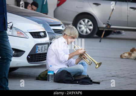 Istanbul, Turkey - September-14.2019: Musician sitting on street in front of car plays trumpet. People who listen are paying. Stock Photo