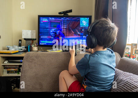 A young boy wearing a headset, playing a computer game on a gaming console. Stock Photo