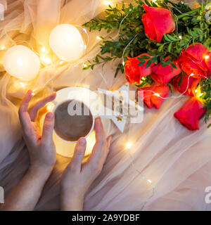 Composition: red roses with boxwood, garlands, candles, star and cup coffee (tea) in hand Stock Photo