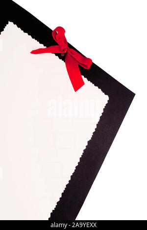 white blank paper with a scalloped edge on top of a piece of black cardboard with a red ribbon. Isolated White Background. Stock Photo