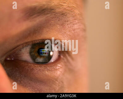 The wide-open eye of a tired man looks at the monitor Stock Photo