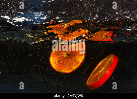 Two slices of fresh tangerine in water with splashes on a black background. Close, horizontal view Stock Photo