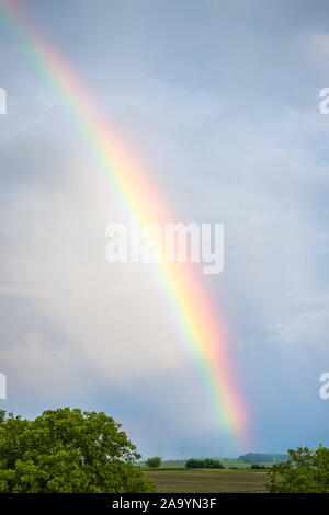 Rainbow over trees and agricultural fields with cloudy sky in background Stock Photo
