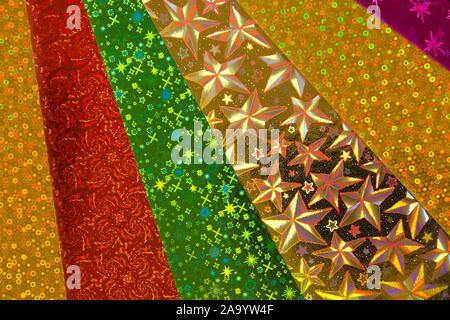 Abstract background of brightly coloured neon holographic gold, purple, silver green and orange paper with stars, dots and swirls. Stock Photo