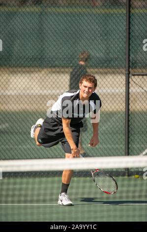 A Johns Hopkins University Men's Tennis player, on an outdoor court on a sunny day, leans forward after swinging the racket during a match with Kalamazoo College, March 24, 2010. From the Homewood Photography Collection. () Stock Photo