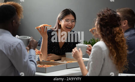 Multiracial colleagues eating delivery pizza and drinking coffee. Stock Photo
