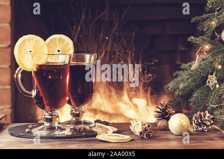 Mulled wine glasses on table in front of burning fireplace. Stock