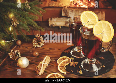 Christmas composition - two glasses with mulled wine on a wooden table near a Christmas tree opposite a burning fireplace. Stock Photo