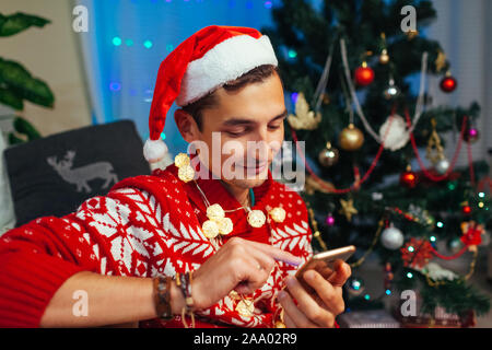 Man texting friends for Christmas using smartphone. Guy celebrating New year alone at home. Mobile operator Stock Photo