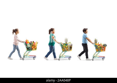 Full length profile shot of three children with shopping carts full of healthy food waling in line isolated on white background Stock Photo