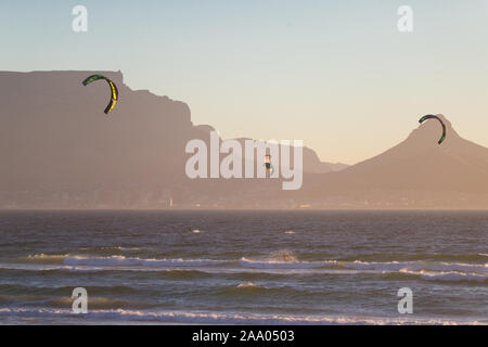 kite surfers in action, riding the waves at sunset at Bloubergstrand, Cape Town, South Africa with Table Mountain and Lions Head in the background Stock Photo