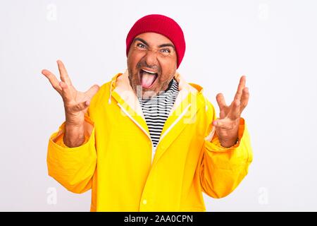 Middle age man wearing rain coat and woolen hat standing over isolated white background celebrating crazy and amazed for success with arms raised and Stock Photo