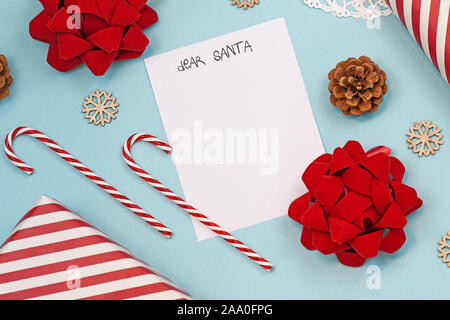 Seasonal Christmas holiday flat lay with concept for children letter to Santa Claus with white empty letter, candy canes, gift box and ribbons on blue Stock Photo