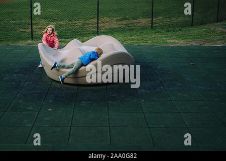Two children play on a merry-go-round at a playground. Stock Photo
