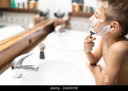little boy shaving like an adult in the bathroom in front of the mirror Stock Photo