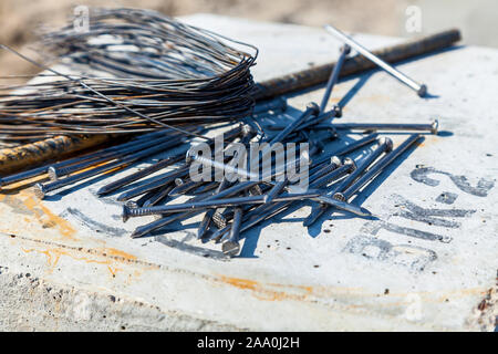 Nails are lying down on the concrete slab next to wire and steel rod Stock Photo