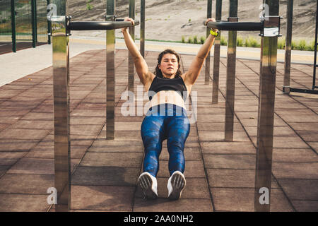 girl trains outdoors in street gym. Training of biceps and triceps. woman parallel bars workout exercise. female athlete exercising on parallel bars Stock Photo