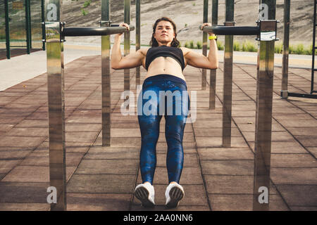 girl trains outdoors in street gym. Training of biceps and triceps. woman parallel bars workout exercise. female athlete exercising on parallel bars Stock Photo