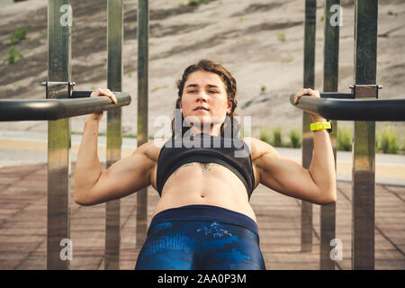 girl trains outdoors in street gym. Training of biceps and triceps. woman parallel bars workout exercise. female athlete exercising on parallel bars Stock Photo