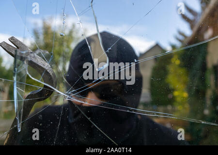 Burglar breaks the window. Burglar with obscured face trying to break the window Stock Photo