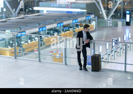 Front of young businessman standing inside the airport looking down on the departure lounge, leaning at the guard railing Stock Photo