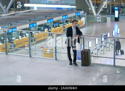 Front of young businessman standing inside the airport looking down on the departure lounge, leaning at the guard railing Stock Photo