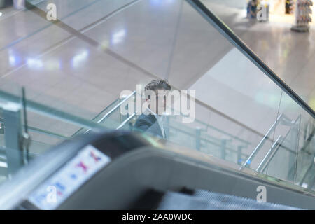 Young attractive businessman going down on an escalator in the airport, looking up Stock Photo
