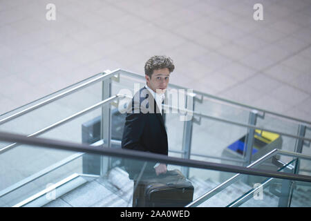 Young businessman going down a stairway with his suitcase, lookin up Stock Photo