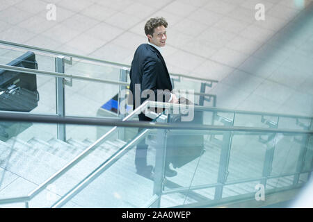 Young businessman going down a stairway with his suitcase, lookin up Stock Photo