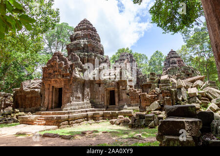 Ta Som temple in rainy season, everything is green and the sky is blue with some scattered white clouds. The ruins are covered with some moss and root Stock Photo