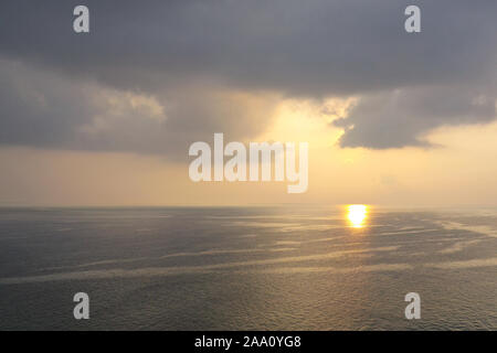 Morning sunrise with penetrating sun rays through black rain storm clouds over the ocean sea Stock Photo
