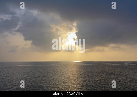 Morning sunrise with penetrating sun rays through black rain storm clouds over the ocean sea Stock Photo