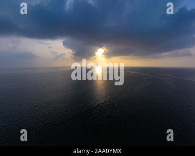 Morning sunrise with penetrating sun rays through black rain storm clouds over the ocean sea Stock Photo