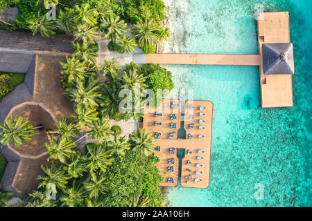 Aerial top down view from drone of a luxurious tropical island paradise resort in Maldives with wooden pier and relaxing area with chairs and tables Stock Photo