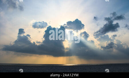 Morning sunrise with penetrating sun rays through black rain storm clouds over the ocean sea Stock Photo