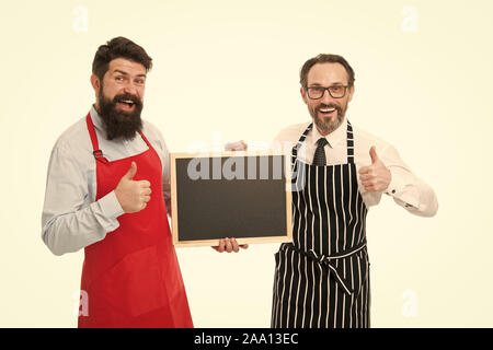 Bar cafe staff. Hiring staff. Men bearded hipster informing you. Men bearded bartender or cook in apron hold blank chalkboard. Bartender with blackboard. Hipster bartender show blackboard copy space. Stock Photo